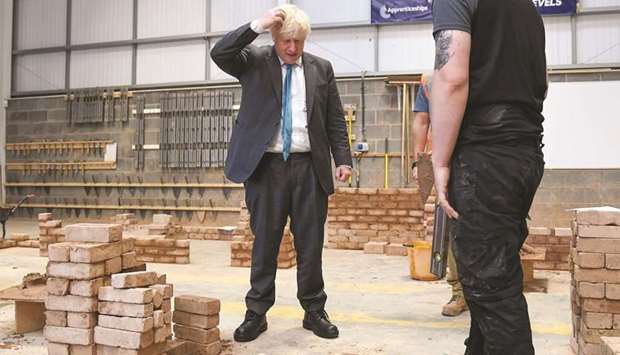 Prime Minister Boris Johnson reacts as he lays bricks whilst talking with students during his visit to Exeter College in Exeter, southwest England, yesterday.