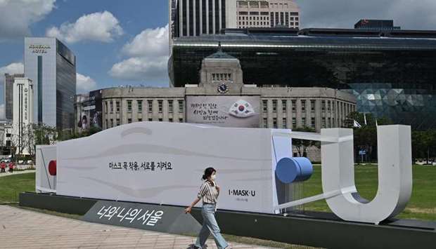 A woman walks past a mask-shaped sculpture in front of Seoul City Hall. South Korea reported 198 new Covid-19 cases yesterday, the 22nd consecutive day of triple-digit increases.