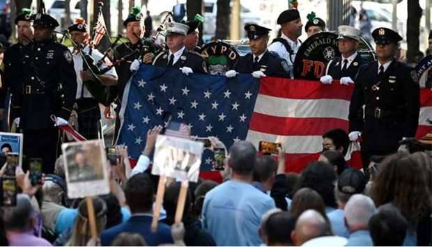 New York police and firefighters hold a US flag as a band plays the US National Anthem at the National 9/11 Memorial.