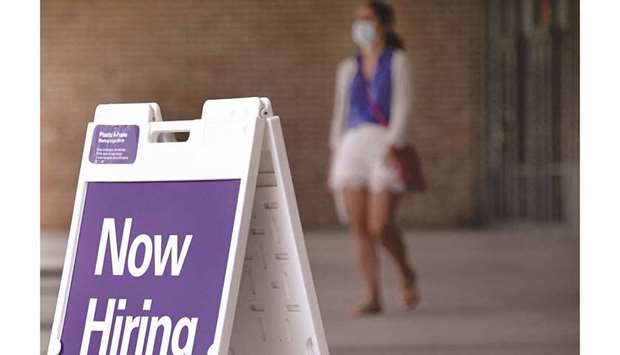 A woman walks by a u201cNow Hiringu201d sign outside a store in Arlington, Virginia (file). The number of Americans filing new claims for jobless benefits fell to the lowest level in nearly 18 months last week, offering more evidence that job growth was being hindered by labour shortages rather than cooling demand for workers.