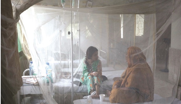 A patient suffering from dengue fever chats with a woman while sitting under a mosquito net inside a dengue and malaria ward at the Sindh Government Services Hospital in Karachi yesterday.