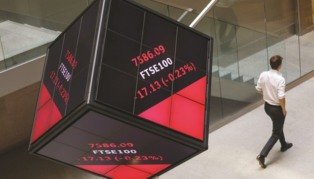 An employee walks past FTSE 100 share price information displayed on an illuminated rotating cube in the atrium of the London Stock Exchange. Britainu2019s mid-cap index u2013 made up of companies that are heavily dependent on the local economy u2013 is down 20% this year, on course for its biggest-ever annual underperformance against the exporter-heavy FTSE 100.