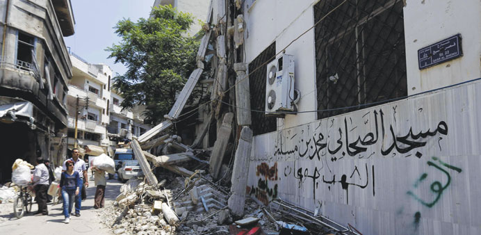 People walk past graffiti sprayed by opposition fighters in the Old City of Homs. The graffiti reads: u201cThe people are starving.u201d