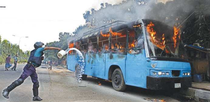 A policeman throwing water at a bus set alight during a protest ahead of a three-day strike, in Dhaka yesterday.