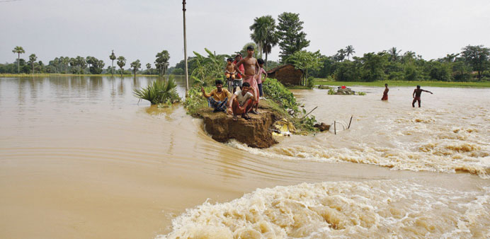 Flood-affected people sit on a broken embankment of a road damaged by flood waters as they await relief supplies in Howrah district of West Bengal.