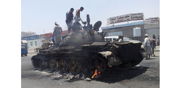  People stand on a tank that was burnt during clashes on a street in Aden yesterday.