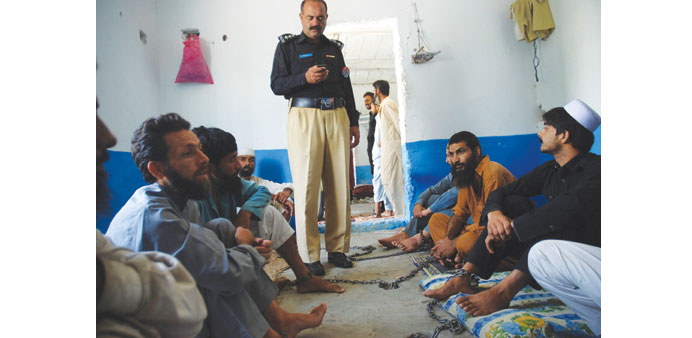 This photograph taken on July 19, shows a police officer standing among chained drug addicts at a healing centre run by a local cleric in Haripur, som