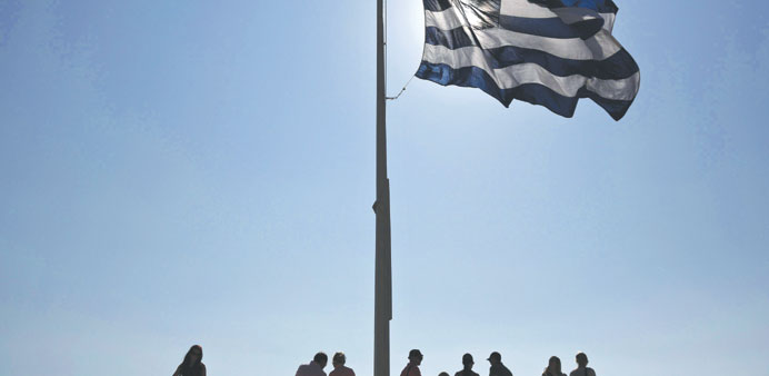 Tourists rest beneath a Greek flag atop the hill of the Acropolis in Athens yesterday. The EU and IMF are unhappy with the progress Greece has made in