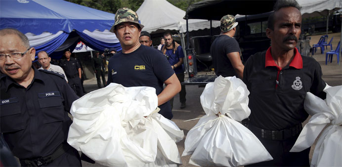 Forensic policemen carry body bags with human remains found at the site of human trafficking camps