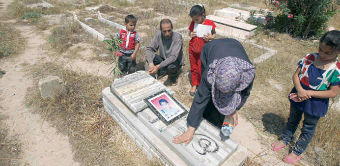 Jamal al-Dura and his children look on as his wife washes down the gravestone of their son Mohamed at the Bureij cemetery in the central Gaza Strip ye