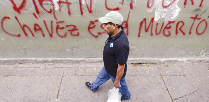 A man walks past a graffiti reading u201c(Say the Truth,) Chavez is Deadu201d in Caracas yesterday.