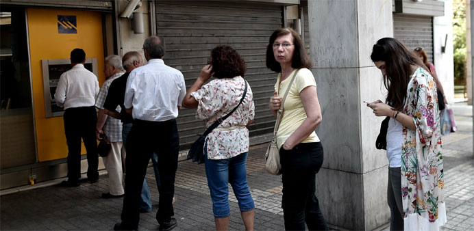 People queue to withdraw cash from an ATM machine in central Athens