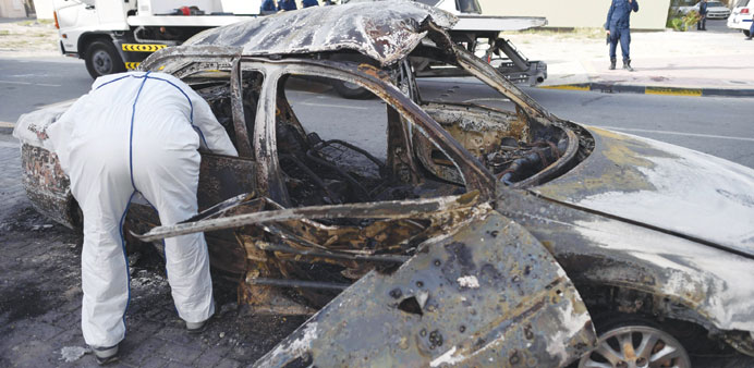 A forensic analyst inspects the destroyed car after the explosion in the village of Mughsha, west of Manama, yesterday.