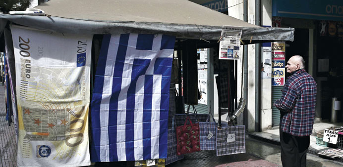 A man looks at the Greek flag and a towel depicting a Euro banknote hanging outside a kiosk in Athens.