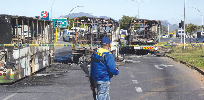A member of the Cape Town Metro Police walks past the charred wrecks of Golden Arrow buses on the road, near the Nyanga township of Cape Town yesterda