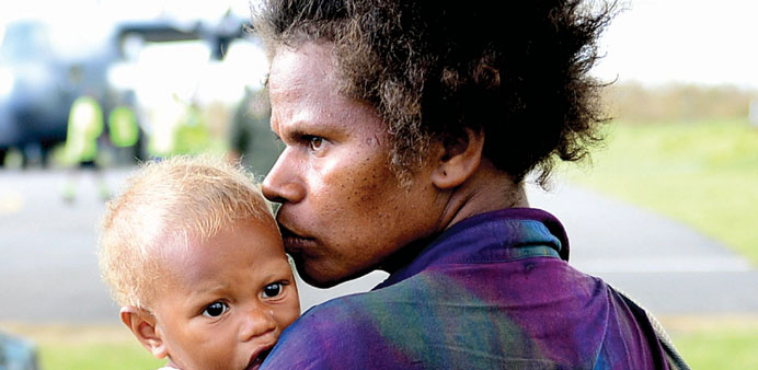 A mother with her child at the Tanna Island Airport before being airlifted to Port Vila hospital. Right: Destruction in Port Vila.