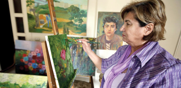 Mariam Saidi paints as she stands in front of an oil painting of her son Maher, who disappeared in 1982 at the age of 15 while fighting near Beirut, a