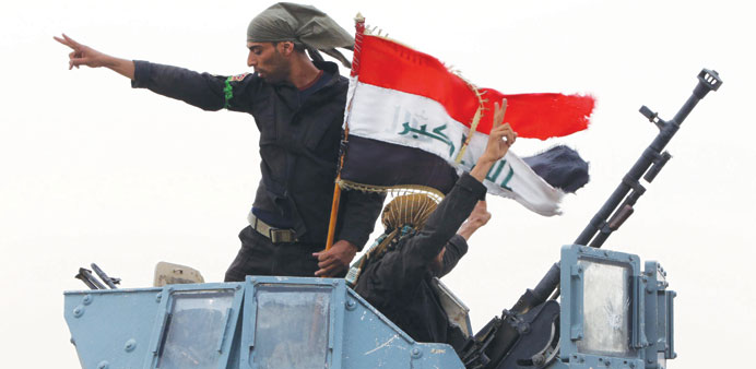 Members of the Iraqi anti-terrorism forces wave the national flag in celebration yesterday after securing a checkpoint from Sunni militants in the vil