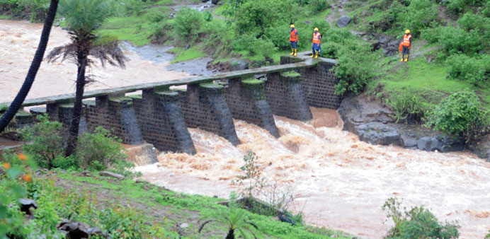 National Disaster Response Force (NDRF) personnel, standing by the banks of a gushing river, keep a lookout for bodies being swept away by the current