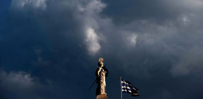 A Greek flag flying next to a statue of Athena in the centre of Athens as rain clouds gather in the sky.