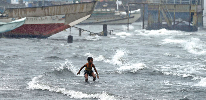 A Filipino boy wades through rising sea water during a downpour at a fish port in Navotas city, east of Manila yesterday.