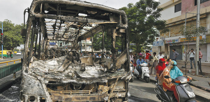 Commuters ride past the wreckage of a bus burnt in the clashes between the police and protesters in Ahmedabad yesterday.