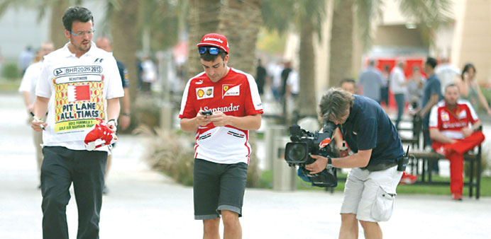 Ferrari Formula One driver Fernando Alonso of Spain (C) checks his mobile phone in the paddock at the Bahrain International Circuit April 18, 2013 REU