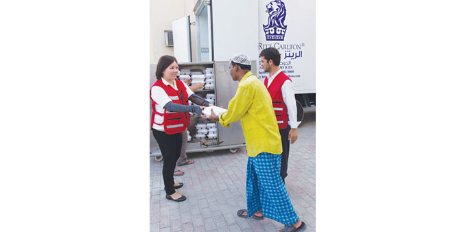A Ritz-Carlton, Doha staffer handing out an Iftar box to a man.