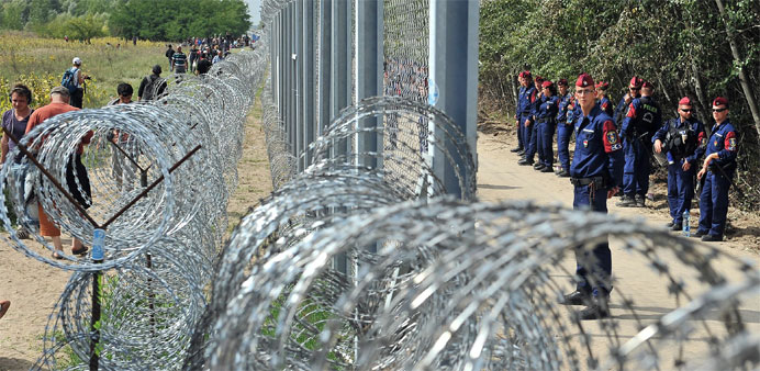 Migrants and refugees walk near razor-wire along a 3-meter-high fence secured by Hungarian police (R) at the official border crossing between Serbia a