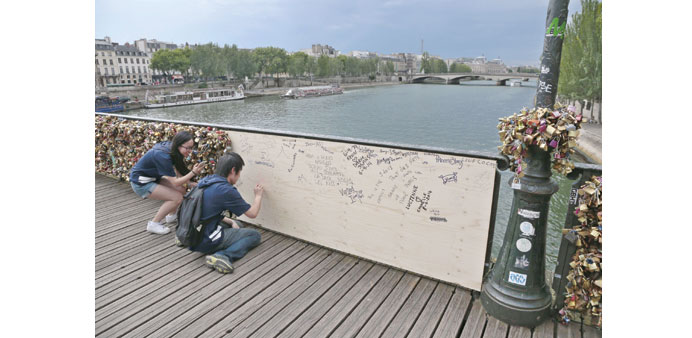 People write inscriptions onto a temporary wooden panel on the Pont des Arts bridge.