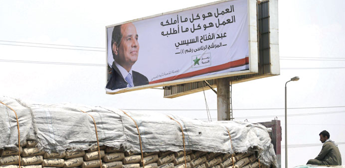 A cement company worker looks on while passing by in a truck as workers install a campaign billboard of presidential candidate Abdel Fattah al-Sisi al