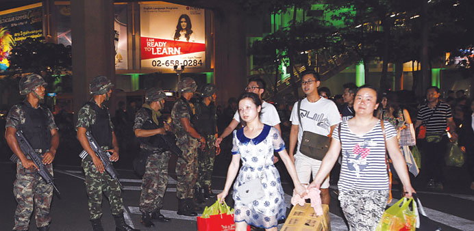 Shoppers walk past soldiers guarding a road in central Bangkok, a day after the Thai army chief seized power in a coup.
