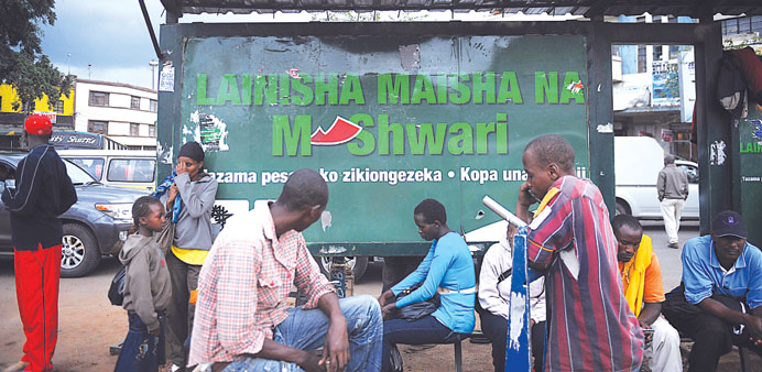 People wait for a bus near an advertisement for the M-Shwari banking initiative.
