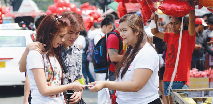 A church volunteer (right) gives out free candy to passersby along a street with vendors selling Valentineu2019s Day items in Manila yesterday.