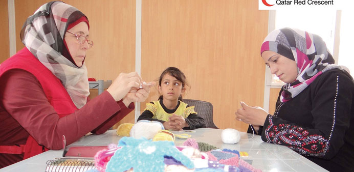 A QRC instructor helps a Syrian woman with needlework