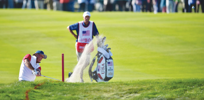 Phil Mickelson of the US (L) blasts out of a bunker on the 18th hole during the second round four-ball matches at the 2015 Presidents Cup at the Jack 