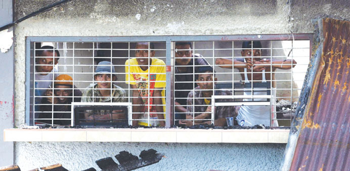 Indonesian inmates stand behind the bars of the burnt Tanjung Gusta prison, following the riot at the prison in Medan, north Sumatra province yesterda