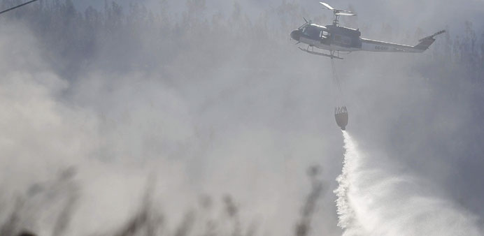 A helicopter dumps sea water on smoldering brush and debris after a fire burned several neighbourhoods in Valparaiso city.